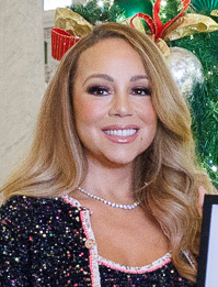 クリスマスツリーの前で黒いドレスを着て微笑むマライア・キャリー