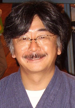 カメラに向かって笑顔を見せる46歳の日本人男性。黒髪だがこめかみあたりは白髪交じりで、口ひげも白くなっている。