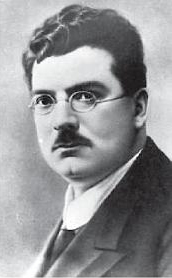丸い眼鏡をかけ、黒い巻き毛と口ひげを生やした中年の白人男性の白黒ポートレート
