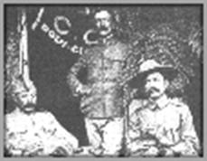 1910年頃のボーイスカウトのイベントで撮影された3人の男性の写真。左端に座っている男性は身元不明、中央に立っているのはバーナム、右端に座っているのはベーデン=パウエルである。3人の前にはテーブルが置かれている。ベーデン=パウエルはステットソン帽をかぶっており、バーナムは帽子をかぶっておらず、左端の男性は質素な帽子をかぶっている。バーナムの後ろ、右側には、半分ほど開いた旗が掲げられている。
