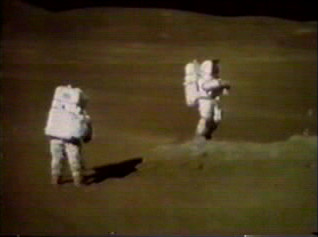 デューク (左) とヤングがプラムの縁にいる様子をテレビカメラで撮影した静止画。デュークはこのとき、「ジョン、君は本当に美しい。この上なく美しい光景だ」と述べた。ヤングはサンプル 61295 が採取された岩の隣に立っている。