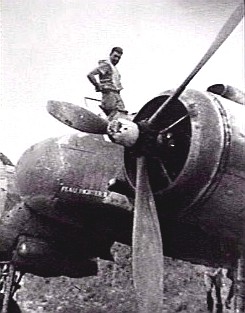 双発軍用機の屋根の上に立つ男性が、カメラを見下ろしている。