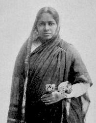 インド人女性が黒いサリーを着て、その裾を頭と肩に垂らしています。彼女は花を持っています。