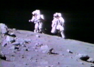 宇宙飛行士のチャールズ・デューク(右)とジョン・ヤングが、ステーション4の角張った縁のクレーターから月面車に向かって歩いている。