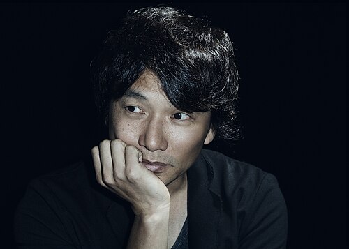 黒いシャツを着た日本人男性が右の方を見て、考え込んでいる。