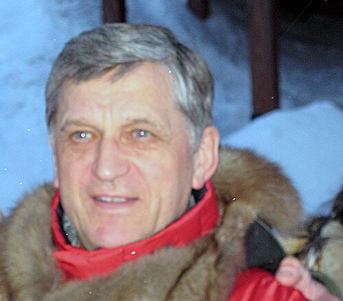 灰色の髪をしており、赤と茶色のコートを着ており、背景には雪が降っている男性。