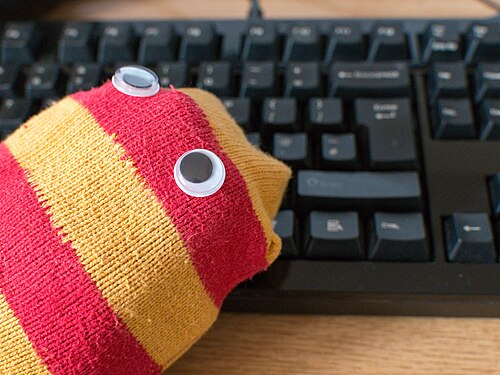 コンピューターのキーボードの前にある目つきの靴下の人形