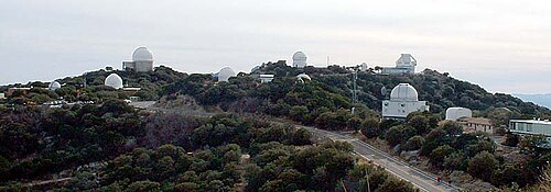 木々や白いドーム型の望遠鏡の建物、そして頂上まで続く道がある山頂のパノラマビュー。