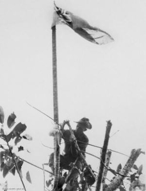 軍服を着た男性がひざまずいて旗竿に旗を掲げている。
