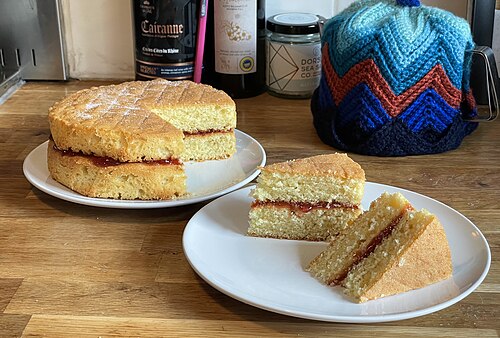 イチゴジャムを詰めた2段のビクトリアサンドイッチケーキ。2つのスライスが準備されており、ケーキの構造を示しています。