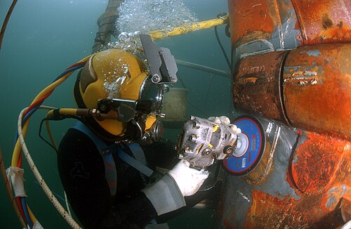 潜水ヘルメットをかぶったダイバーが潜水艦の修理パッチを研磨している