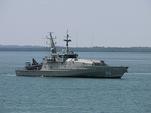 灰色の軍艦が航行中。背景に陸地が見える。