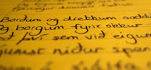 一見黄色い紙に書かれた黒い手書きの文字の写真。上部と下部はぼやけているが、中央の縦線ははっきりしている。
