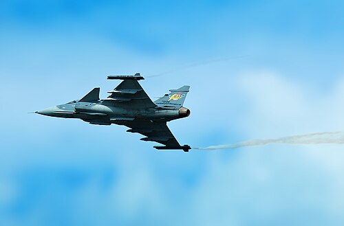青い曇り空を背景に、翼端渦を発生させながら飛行中のジェット機を後方下面から3/4から見た図。