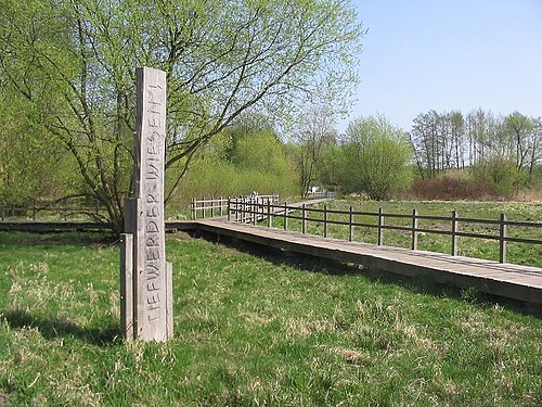 「Tiefwerder Wiesen」と彫られた木製の標識。芝生エリアを通る遊歩道の始まりを示しています。
