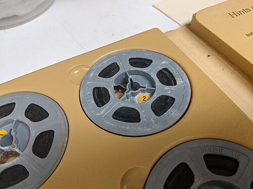 アルバムに収められた 8mm ホームムービーのフィルム リールのクローズ アップ。灰色のプラスチック リールは、フィルムに広がった白い粉状の物質で覆われています。