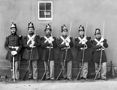 6 人のアメリカ海兵隊員が一列に並んでいる白黒写真。5 人は南北戦争時代のライフルを持ち、1 人は下士官の剣を持っています。
