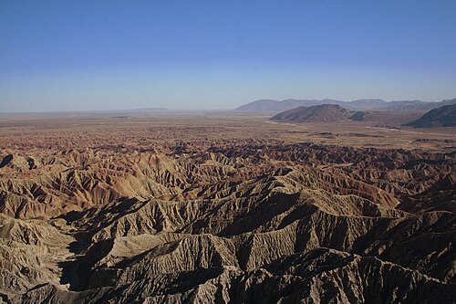 写真は荒涼とした砂漠地帯を写したもので、いくつもの峡谷があり、青い空を背景にしている。