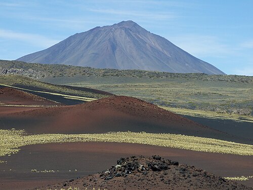 火山の噴石丘。背景には円錐形の山がそびえている。