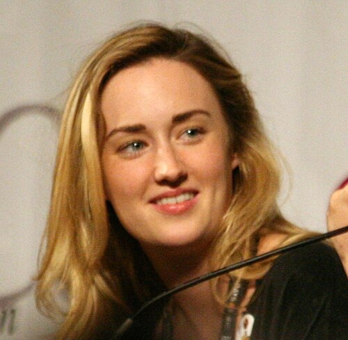 30代前半の金髪女性がカメラの外の何かに微笑んでいる
