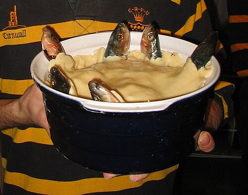 青い陶器の皿にスターゲイジーパイが盛られており、ショートクラスト生地の蓋から6匹の魚が顔を出して上を向いている。