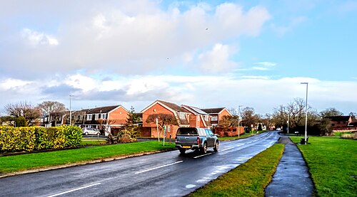 露に濡れた緑の草に囲まれた、1970年代風の農家風レンガ造りの家々のそばを、車が通り過ぎる。