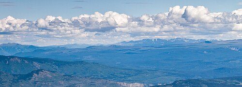背景と前景に山々があり、植物が生い茂る斜面の上にそびえる緩やかな傾斜面。