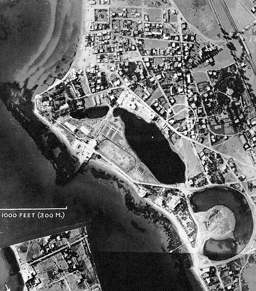 水が満たされたトーラス型の入り江がある海沿いの都市部の白黒航空写真。