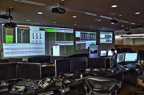 コンピューターが並ぶ暗いオフィス。財務データの画面が壁一面に並ぶ