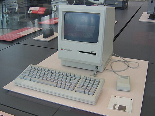 博物館の展示ケースに展示されている Macintosh Plus モニター、キーボード、マウス、フロッピー ディスク