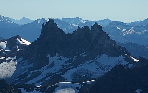 前景には氷河の上にそびえる暗く険しい山、背景には氷河に覆われた山々。