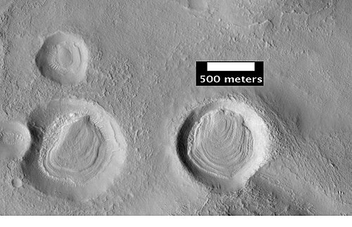 HiWish プログラムの HiRISE が撮影したクレーター内の層。おそらくこの層で覆われていたと思われるが、保護されたクレーター内部を除いて、現在では層は浸食されて消失している。
