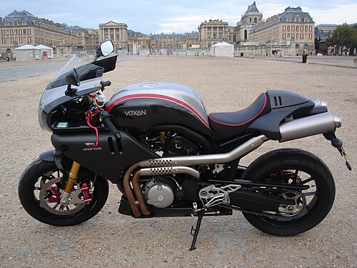フランスの宮殿を背景に、前景に黒と銀の流線型のバイクが描かれている
