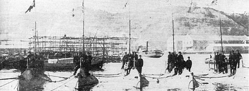 5隻の潜水艦が並んで停泊し、その上に人が立っている