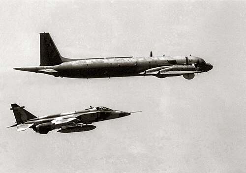 4基のターボプロップエンジンを搭載した航空機の後ろに随伴する、胴体の下に外部燃料タンクを搭載したジェット機の白黒写真。