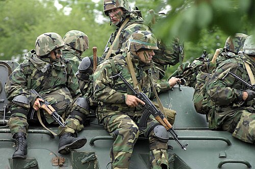 迷彩服を着て顔にペイントを施した兵士6人が、緑色の車両の上に座っている。