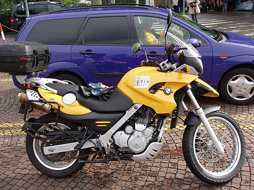 オプションのトップボックスを装備した黄色のBMW F650GSが青い車の隣に駐車されている