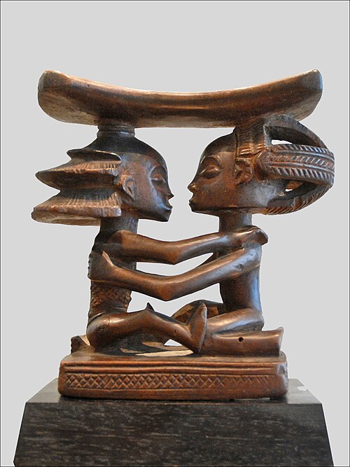 Headrest; 19th century; wood; height: 18.5&nbsp;cm (7.3&nbsp;in), width: 19&nbsp;cm (7.5&nbsp;in), thickness: 8&nbsp;cm (3.1&nbsp;in); Musée du quai Branly (Paris). This headrest presents 19th century Luba hairstyles, as well as the long limbs, bent-back legs, cylindrical torso and dynamic pose typical of the artist who made it