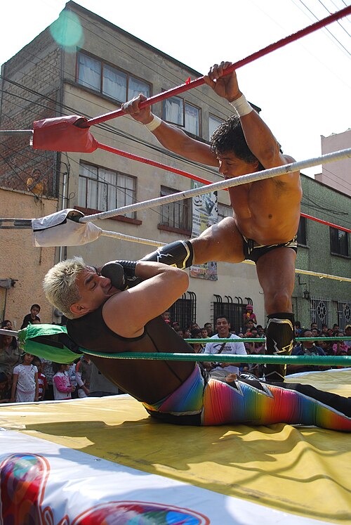 メキシコのレスラーが座っている相手の喉に足を置いている。