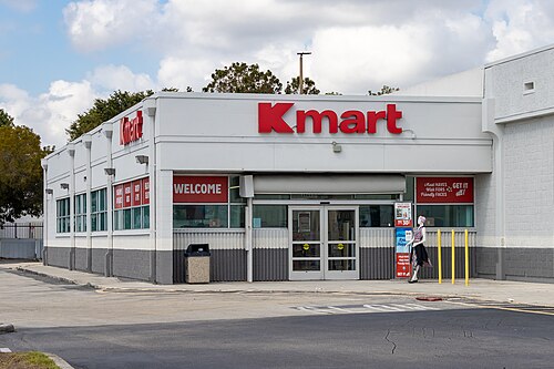灰色の平屋建てのショッピングビルで、入り口の上には「Kmart」の看板が出ている。この店舗はショッピングセンターの一角を占めている。