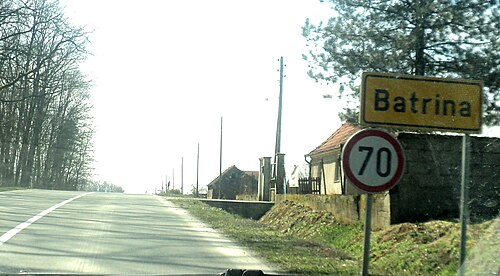 草地の縁と右側にいくつかの家がある道路。右手角に時速 70 キロの標識があります。