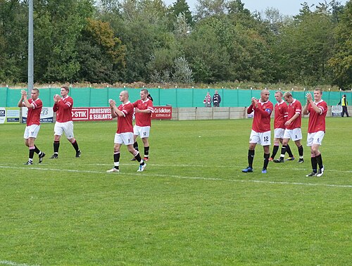 試合後、ペナルティエリアの端に立つFCユナイテッドの選手8人。うち6人がファンに拍手を送っている。