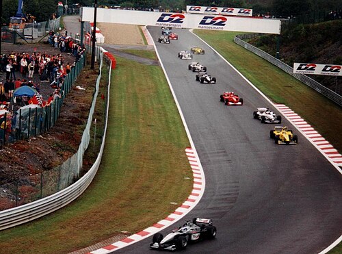 最初の黒と銀の車、ミカ・ハッキネンが、濡れたトラックで10台のF1カーのフィールドをリードしています。