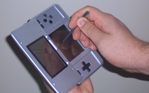 ある人が、片手に携帯型ビデオゲーム機を持ち、もう片方の手に筆記具を持っています。