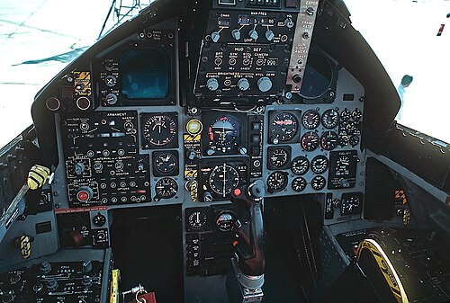 円形のダイヤルとゲージを備えたジェット戦闘機のコックピット: 操縦桿はパイロットの脚がある場所の間から突き出ています。