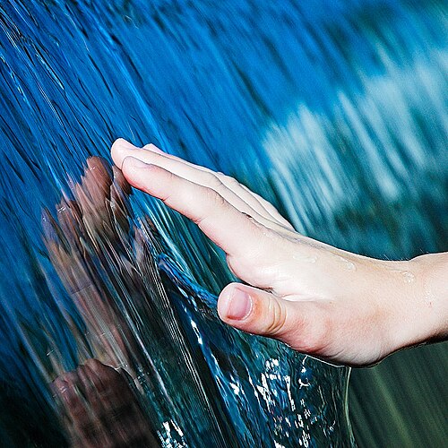 流れる水が手に張り付いている写真。表面張力によって、水の流れと手の間に水の膜が形成される。