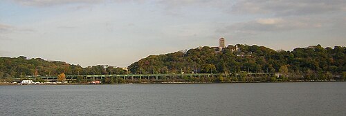 ハドソン川から見た公園の眺め。右側の丘の上にはクロイスターズ美術館が見える。緑色の高架道路はヘンリー・ハドソン・パークウェイ。