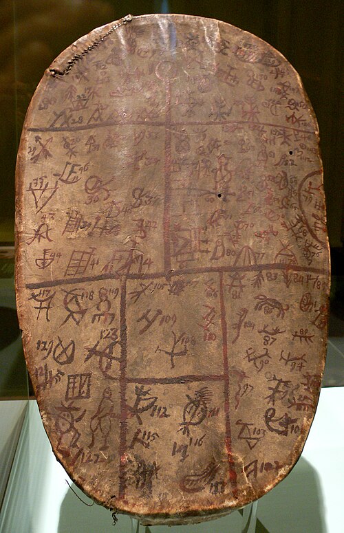 博物館に展示されている、色褪せた茶色と赤色の模様が表面を覆い、塗装された線で区画分けされた楕円形の革製ドラム。