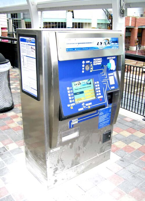 駅のプラットフォームにある銀色と青色の券売機。支払いオプションとデジタル画面が見える。