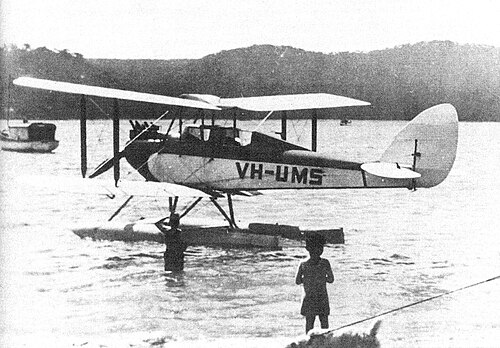フロートに乗った単発複葉機が水上に駐機しており、前景には 2 人の少年がいます。